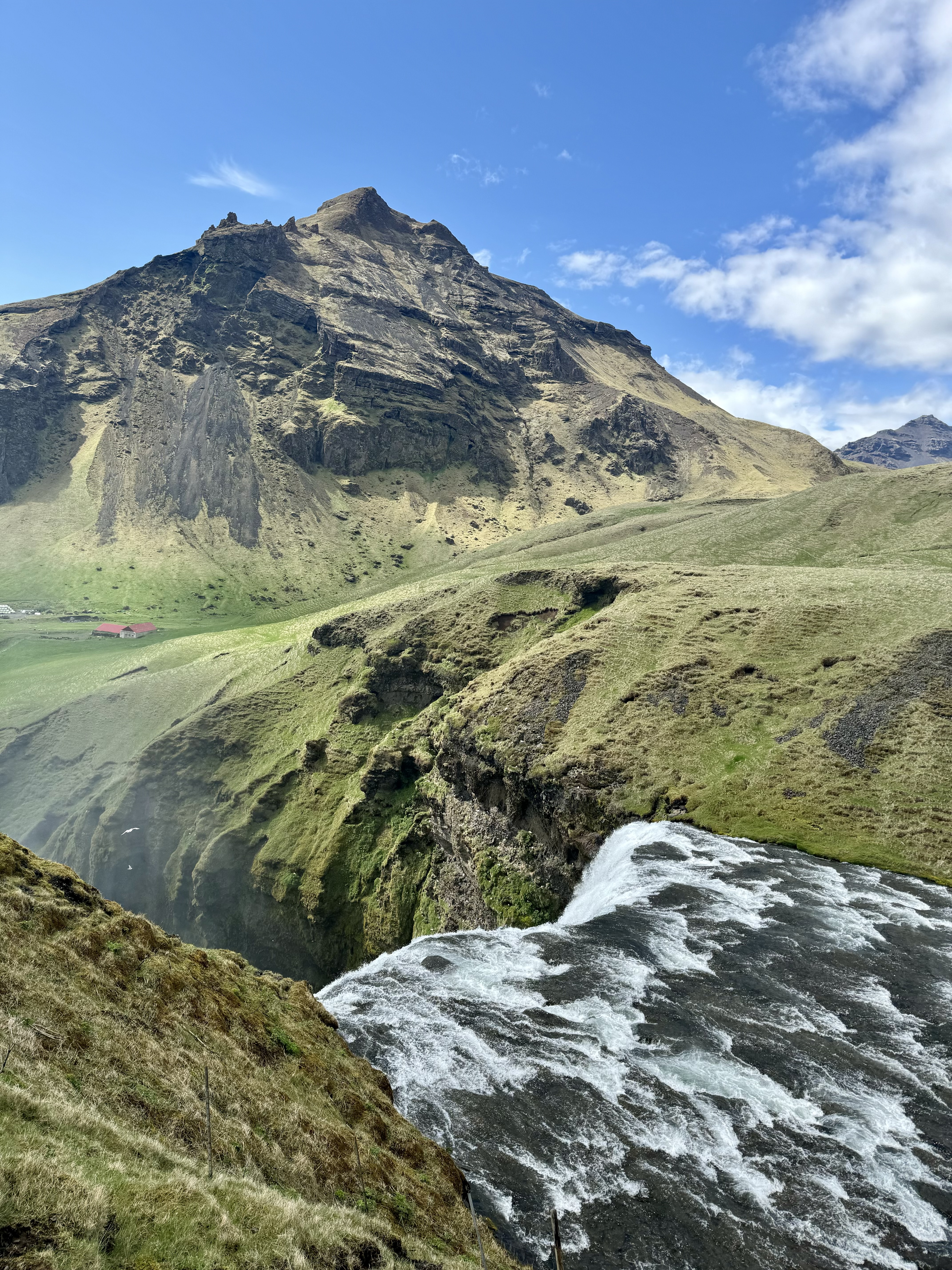 Skogafoss waterfall - a view from the top of a waterfall overlooking green mountains