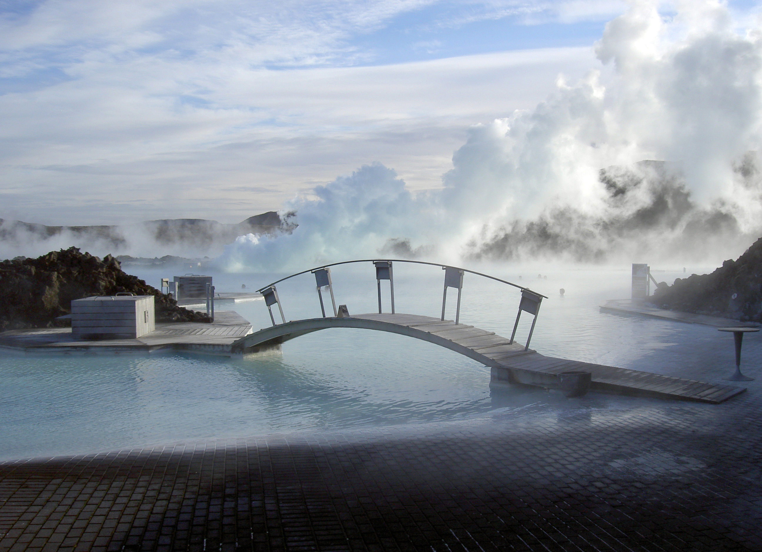 Blue Lagoon - bleu water and a bridge over rocks with steam in the background