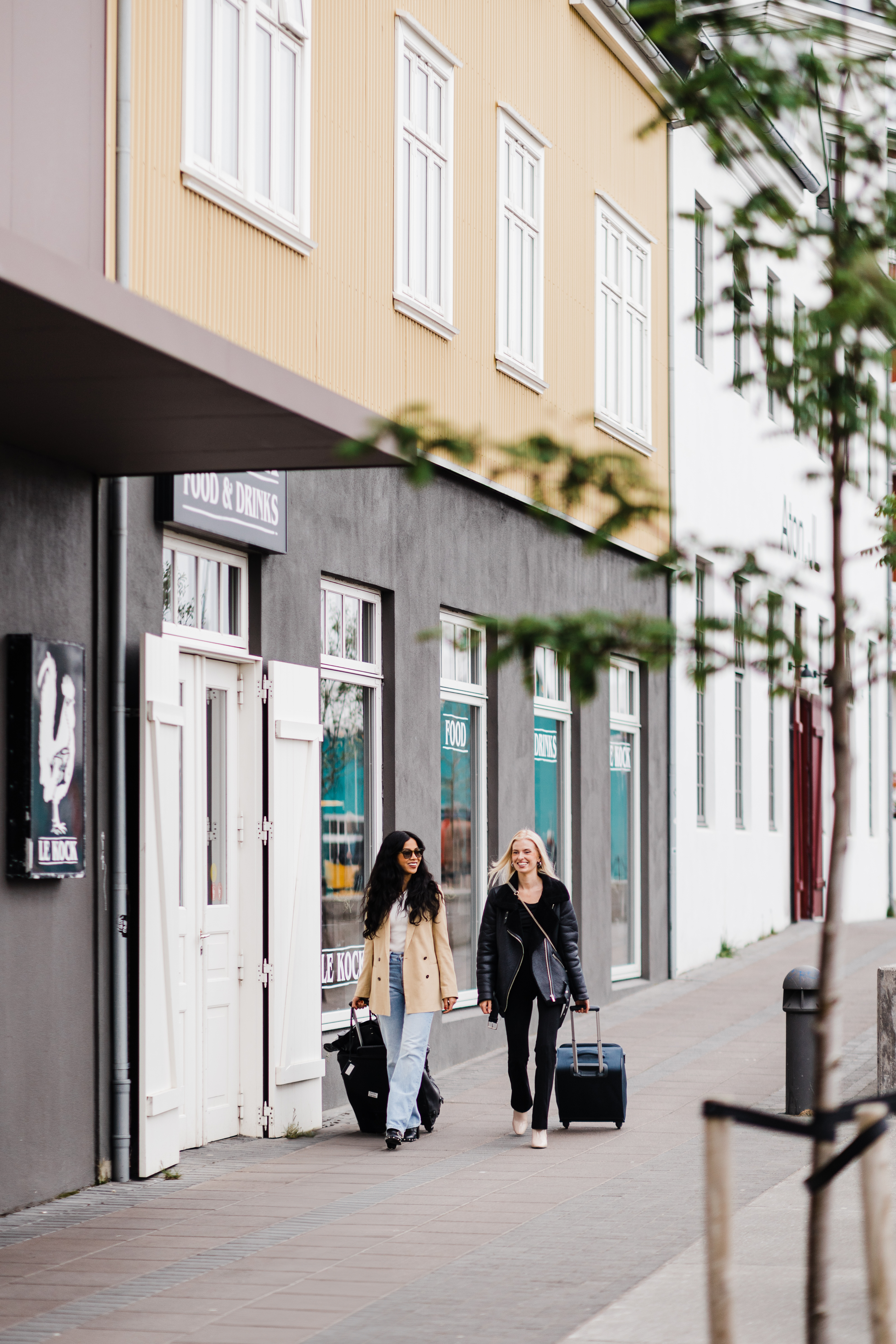 Hotel Exeter - two people walking with suitcases on a road next to a yellow building