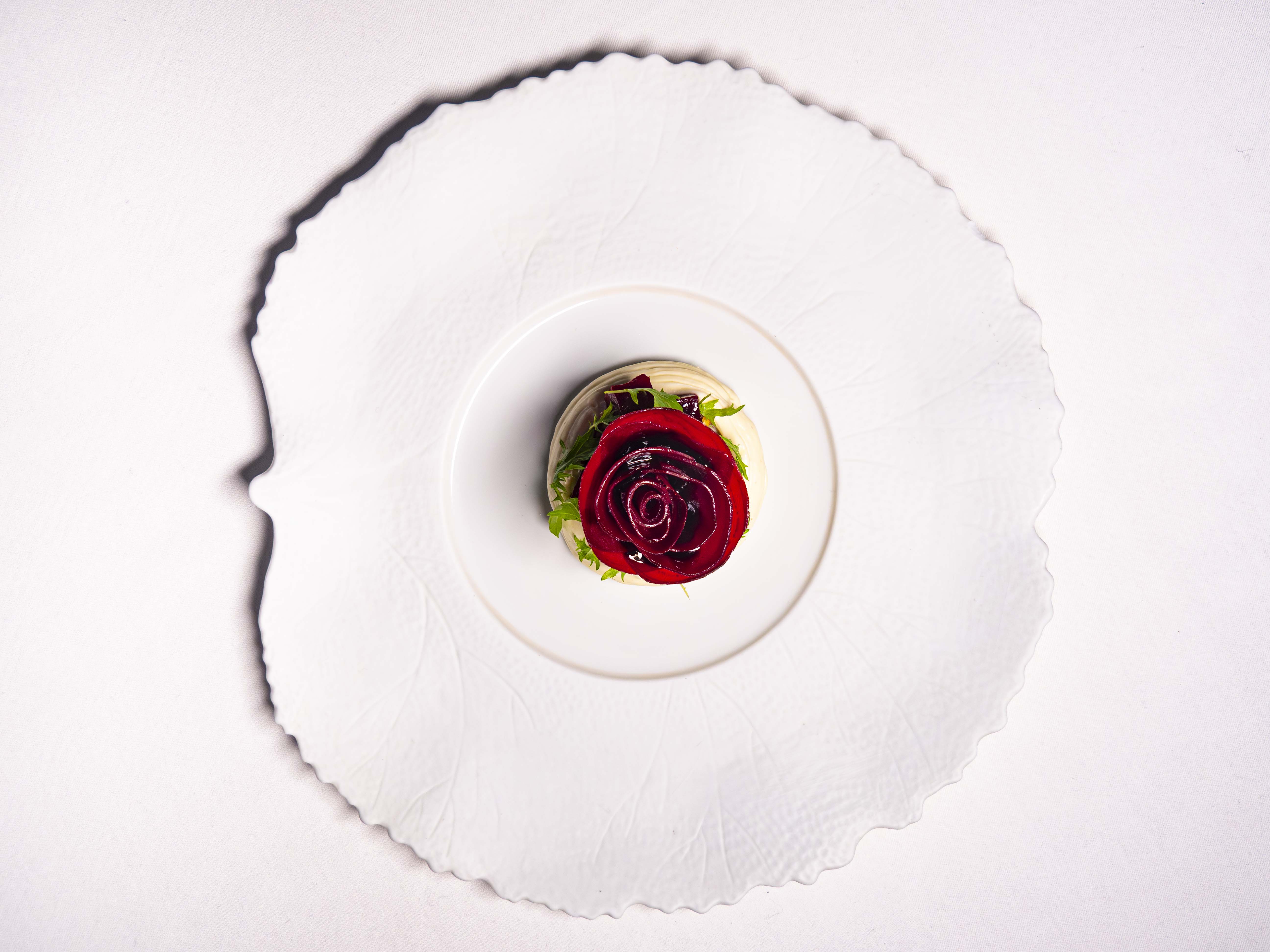 Le Cordon Bleu London -  A top-down view of an elegantly presented dish with sliced beetroot arranged in the shape of roses on a white plate, surrounded by leafy greens and a light drizzle of dressing.