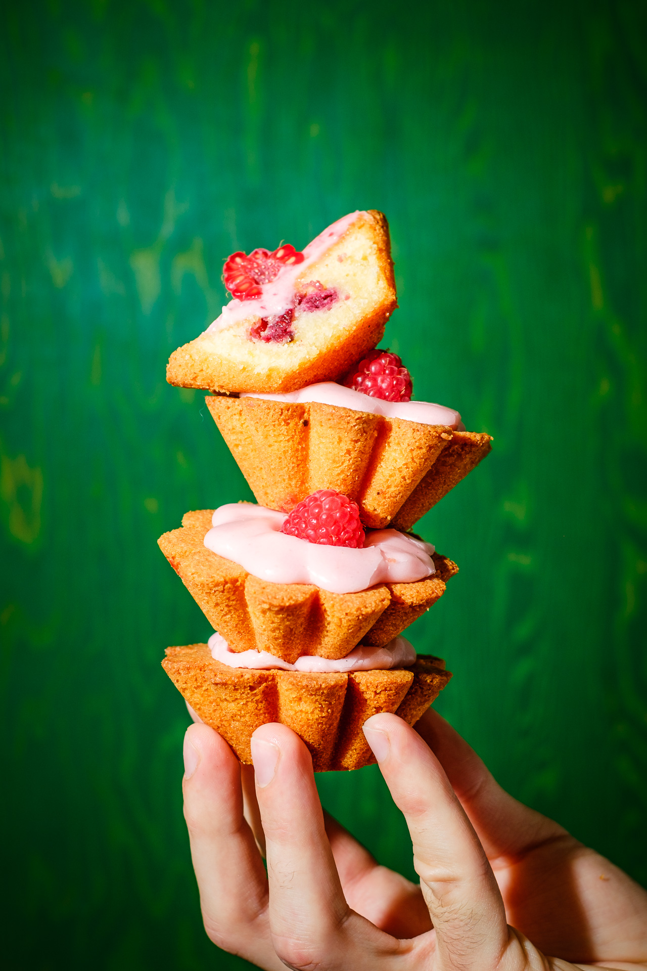 best london artisanal bakeries - a hand holding four raspberry tarts stacked on top of each other in front of a green background at Toad bakery