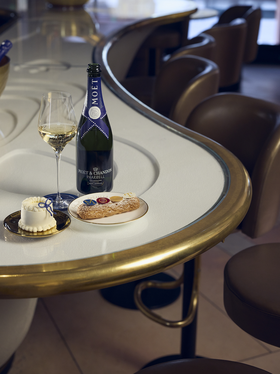 Pharrell Moët & Chandon Harrods Pop-Up - a glass and bottle of Moët & Chandon Champagne alongside a small white celebration cake and eclair