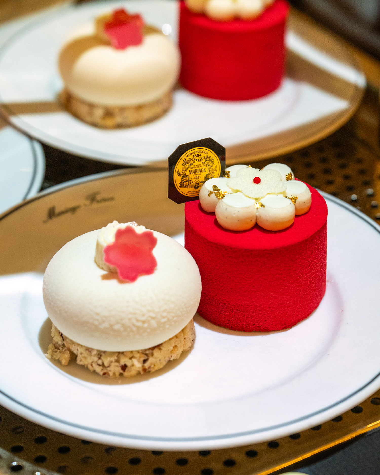 Mariage Frères Japanese floral teas spring - Two delicate pâtisseries featuring cherry blossom designs, one with a smooth white exterior and the other with a vibrant red exterior, placed on a white plate with the Mariage Frères logo.