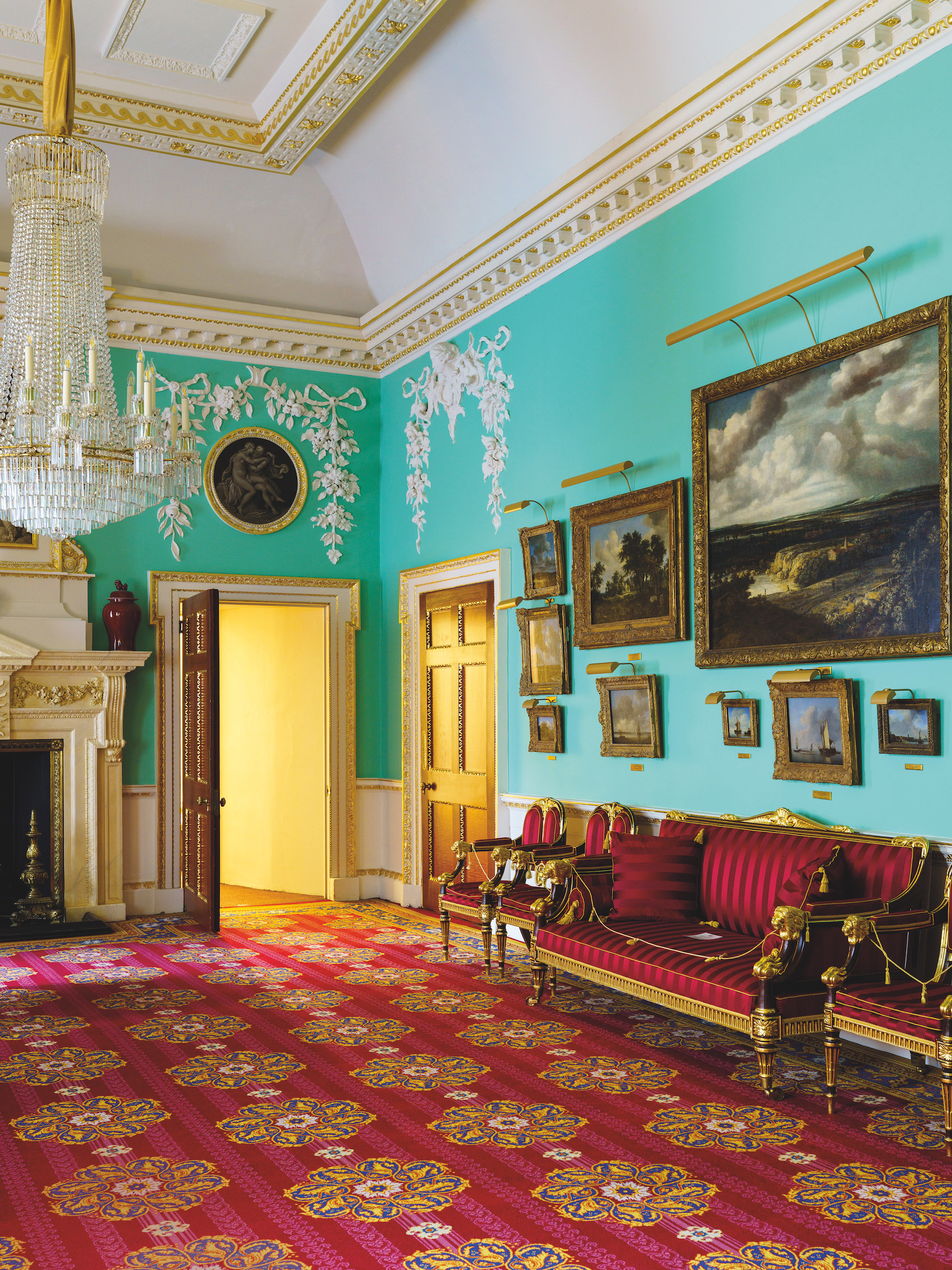 Inside Mansion House Lord Mayor Residence - A colourful room featuring turquoise walls and a chandelier. There are artworks on the walls, and plush red upholstered furniture is arranged around the room. The rich carpet pattern contrasts with the bold colour of the walls.