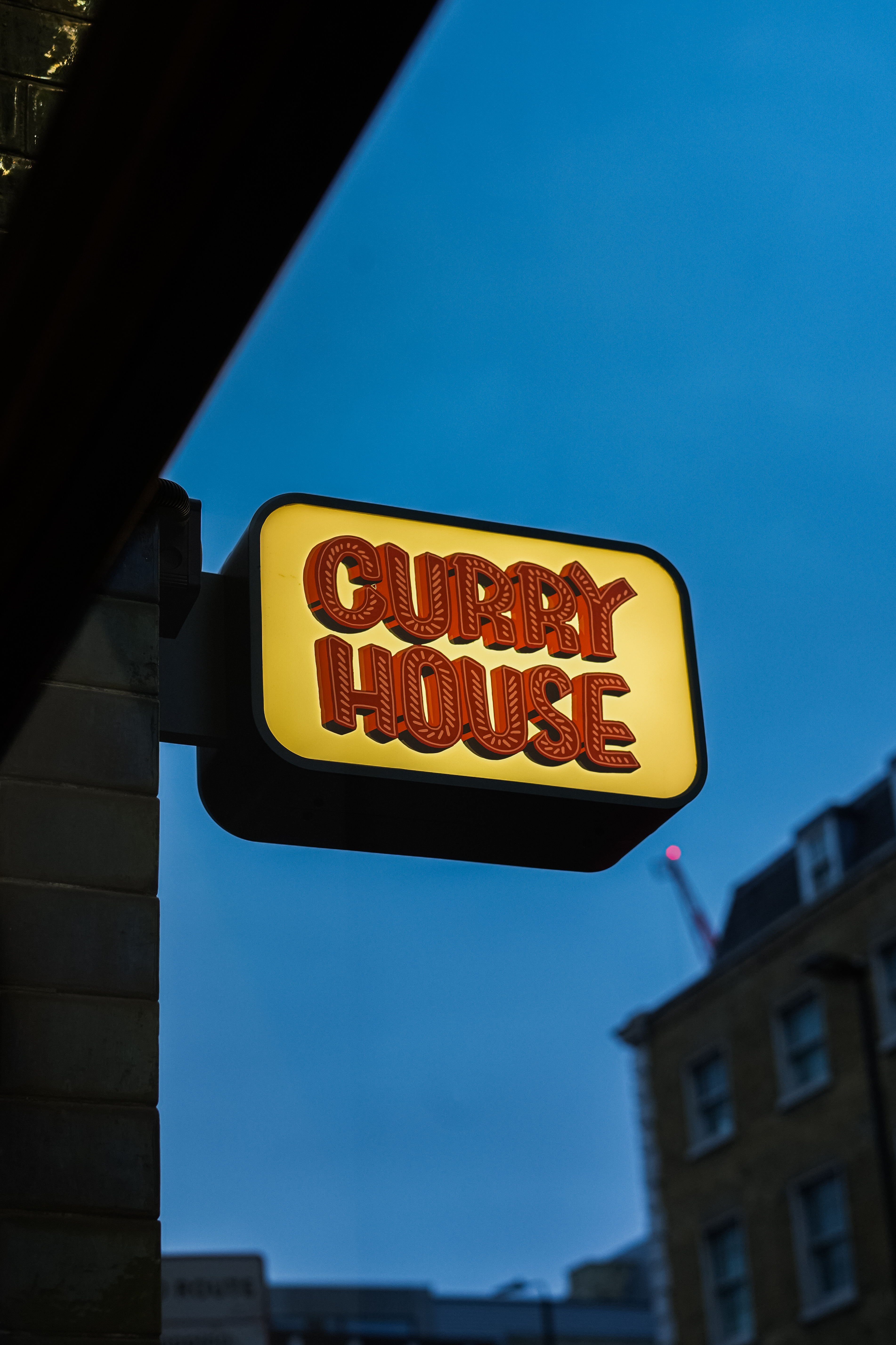 Tamila Restaurant Kings Cross - a yellow and red neon sign reading curry house in front of a blue sky