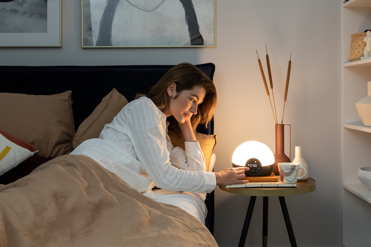 Effective Products Deeper Sleep - a woman sat in bed with a lumie clock alight next to her on a bedside table