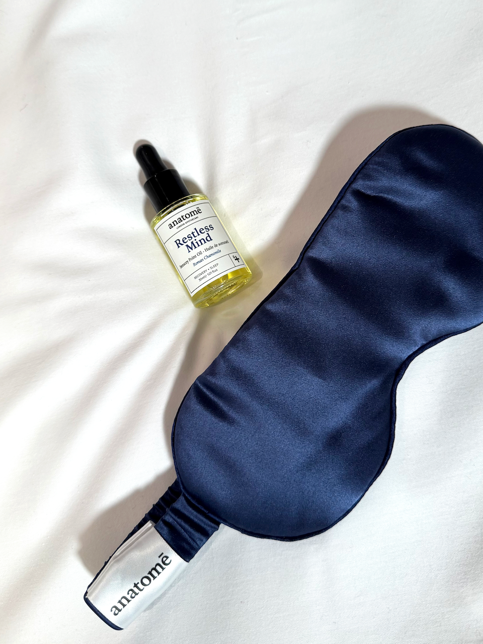 Effective Products Deeper Sleep - a dark blue sleep mask and a dropper bottle of oil on a white sheet