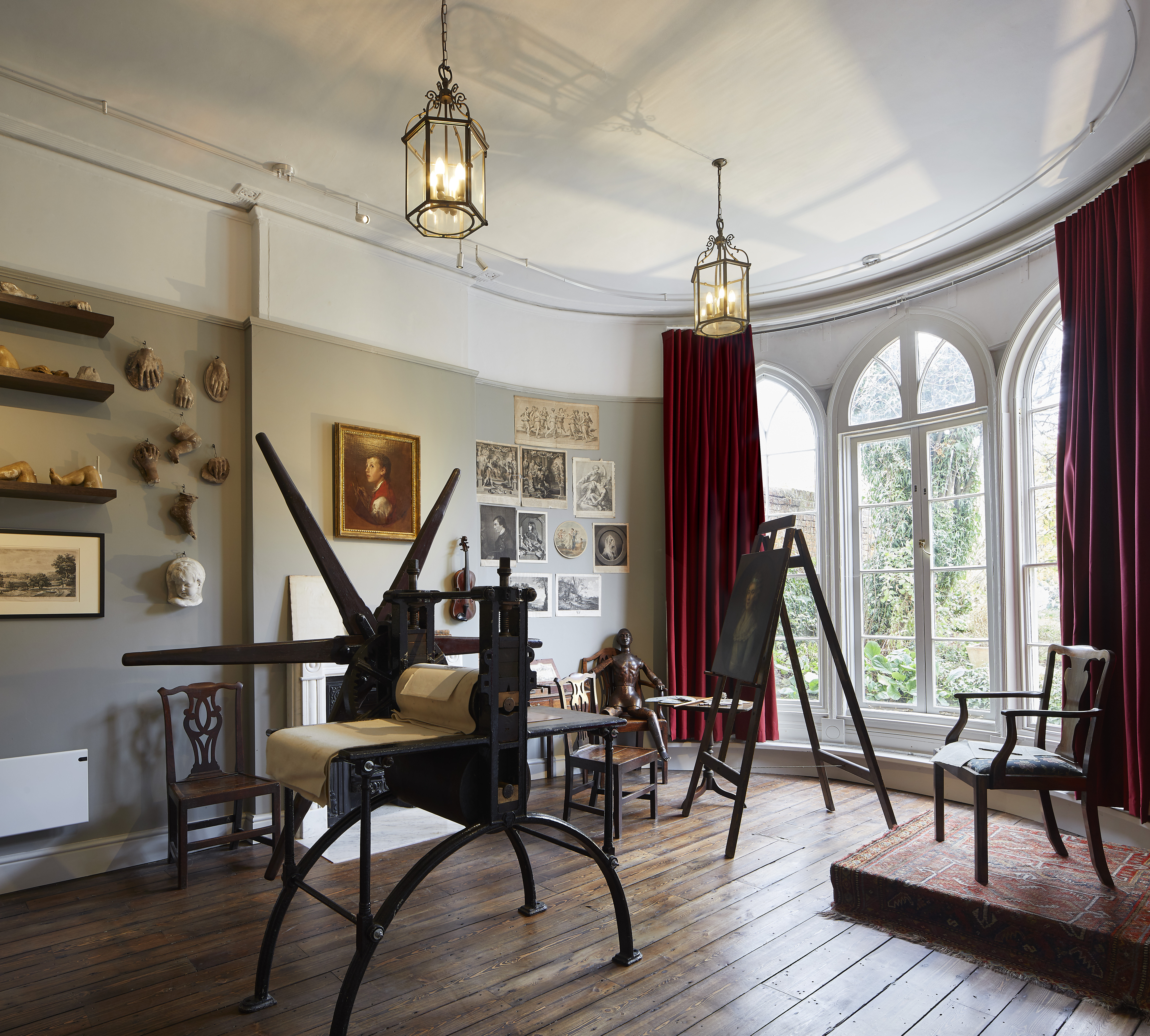 The Painting Room in Gainsborough 's House, filled with paintings, easels and a printing machine.
