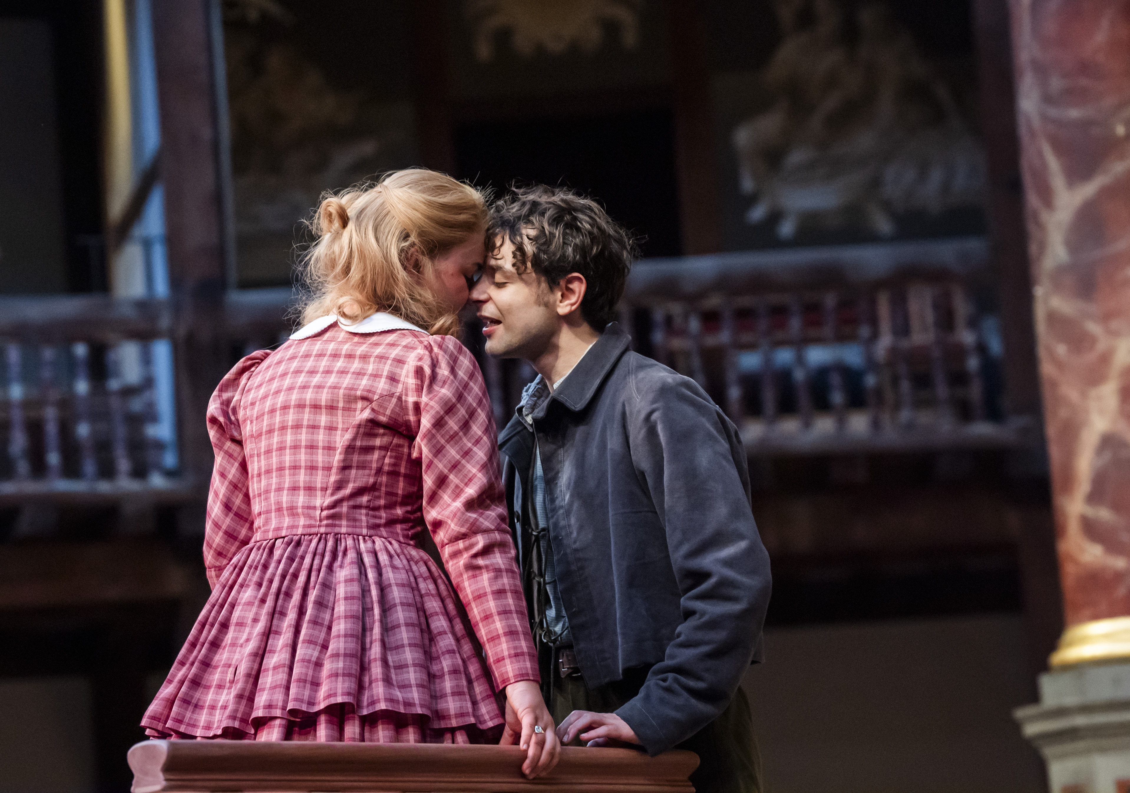 Juliet in red gingham dress holds hands with her face to Romeo