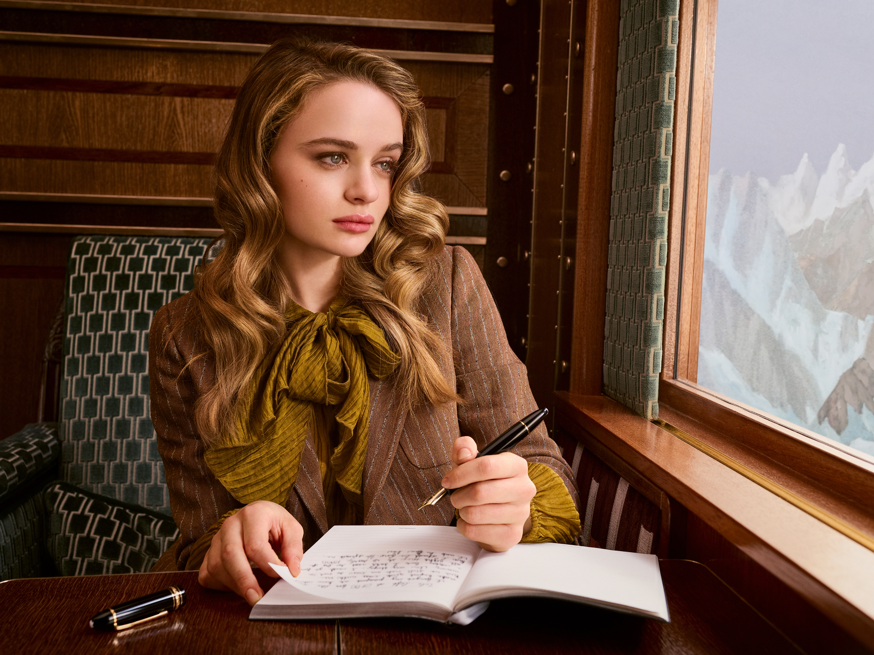 Joey King sits in a train carriage looking out at the mountain landscape in Wes Anderson's campaign film for Montblanc.
