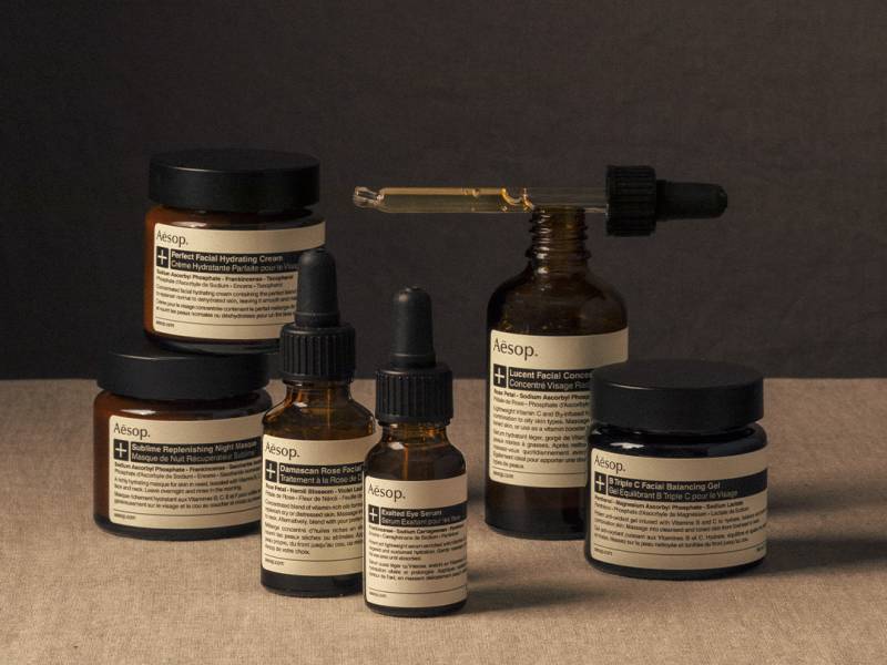 Aesop - brown bottles of skin and hair treatments with white labels and a pipette with product in it