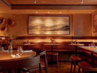 Art restaurants in London - warmly lit restaurant interior of Lolo in Bermondsey featuring wooden tables and cushioned bench seating. A large framed landscape painting serves as the focal point.